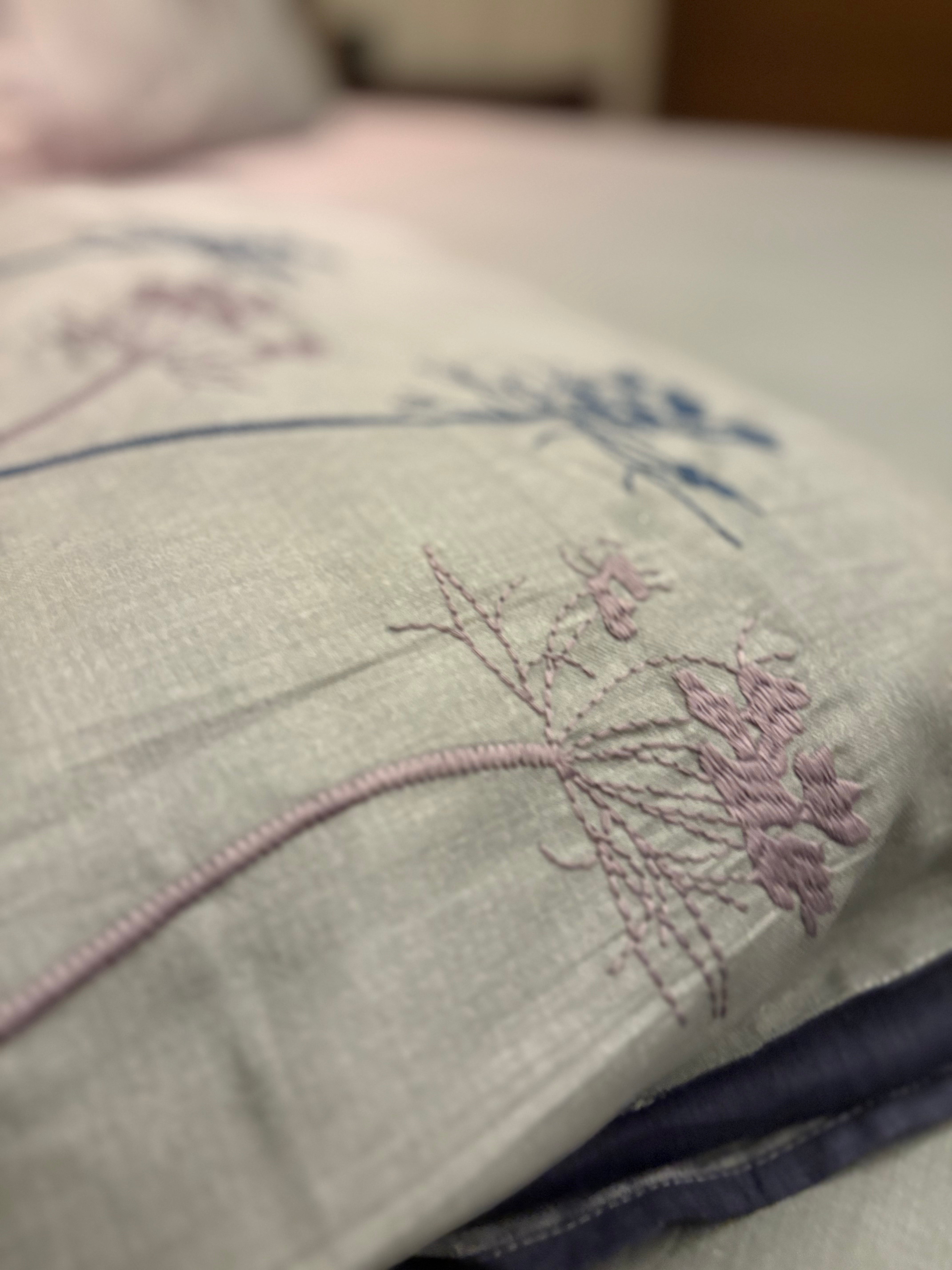 A close-up of the Percale Ombre 250 TC Bedsheet + Pillow Cover Pair Set (King Size), featuring delicate ombre floral patterns in purple and blue on 100% cotton, with a blurred bed and pillow in the background for a luxury hotel vibe.