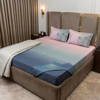 A bed with a pink-to-blue gradient ombre duvet, floral decorative pillows, a cream throw blanket, and our Navy Blue Ombre Percale 250 TC Bedsheet + Pillow Cover Pair Set (King Size) from the Ombre Bedsheet Collection.